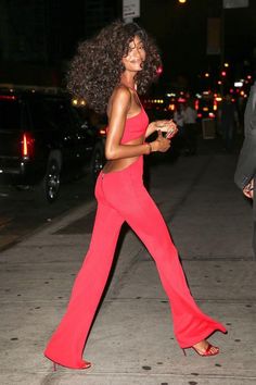 a woman in a red jumpsuit is walking down the street with her hand on her hip