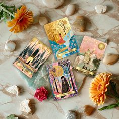 four cards are laying on the ground next to some flowers and rocks with an orange flower