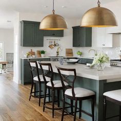 a kitchen with green cabinets and white counter tops, gold pendant lights over the island