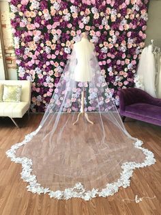 a bridal veil is on display in front of a floral wall with purple and white flowers