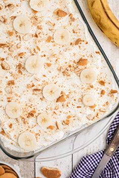 a banana pudding in a glass dish on a white table next to some cookies and bananas