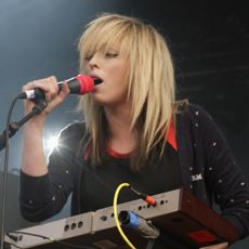 a woman singing into a microphone while standing in front of a keyboard on stage at a music festival