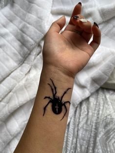 a woman's hand with a black spider tattoo on her left wrist and right arm