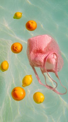 a pink hat floating on top of water next to oranges