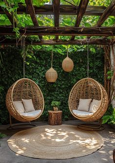 two hanging chairs in the middle of a patio with greenery on either side and round rug underneath them