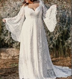 a woman in a long white dress standing on a dirt road with her arms outstretched