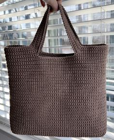 a hand holding a brown crocheted bag on top of a window sill