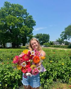 a woman holding a bouquet of flowers in front of a field full of wildflowers