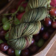 two skeins of yarn sitting on top of grapes in a wooden box with green and red colors