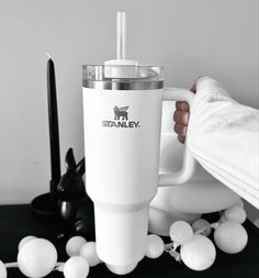 a person holding a white coffee mug with the stanley logo on it next to balloons and candles