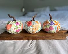 three painted pumpkins sitting on top of a wooden board in front of a bed