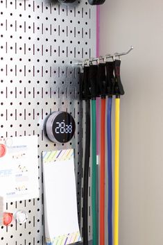 there is a clock that is on the wall next to many different colored cords and clips