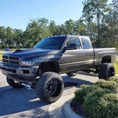 a large gray truck parked on top of a parking lot next to bushes and trees