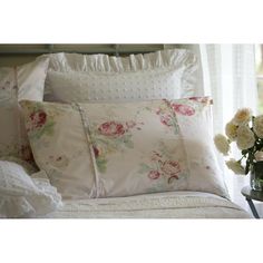 a bed topped with lots of pillows next to a vase filled with flowers and greenery