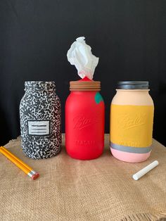 three mason jars sitting on top of a table next to a pencil and paper towel