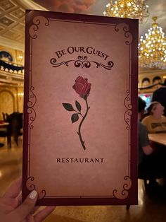 a person holding up a card with a rose on it in front of a chandelier