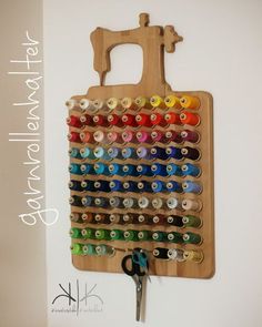 a wooden cutting board with scissors and spools of thread hanging on the wall