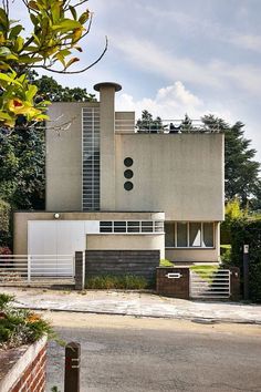 a modern house is shown from the street in front of trees and bushes on either side of the road