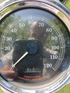 a close up of a speedometer with trees in the backgroud and grass behind it