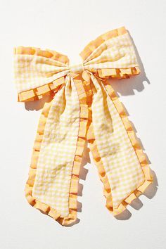 a yellow and white checkered bow tie on a white surface with shadow from the camera