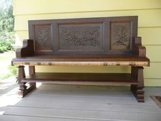 a wooden bench sitting on top of a porch next to a yellow wall and grass