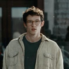 a young man with glasses standing in front of a building