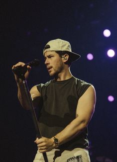 a male in a black shirt is holding a microphone and standing on stage with lights behind him