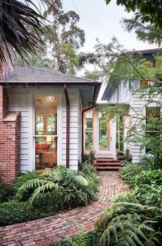 a brick walkway leads to the front door of a white house surrounded by greenery