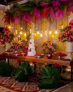 a table topped with a white cake covered in lots of pink and orange flowers next to potted plants