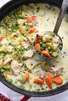 a ladle full of soup with peas, carrots and meat in it on a table