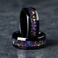 two black rings with multicolored opal inlays sitting on top of each other