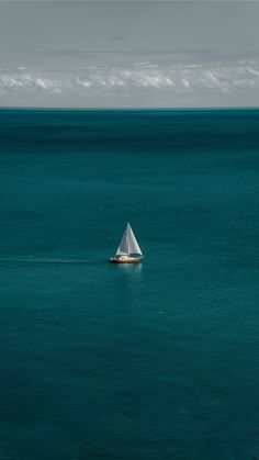 a small sailboat in the middle of an ocean with blue water and white clouds