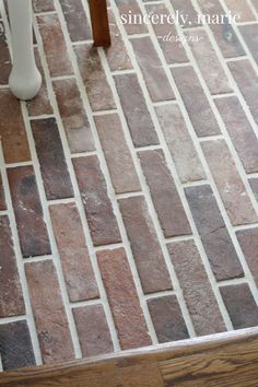 a white vase sitting on top of a wooden table next to a chair and tiled floor