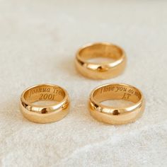 three gold wedding rings with the names of two people and one is inscribed on them