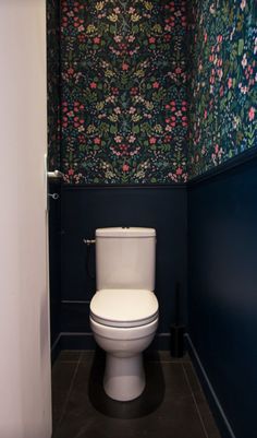 a white toilet sitting inside of a bathroom next to a wall papered with flowers