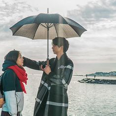 two people standing under an umbrella near the water