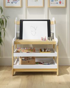 an easel with art supplies on it in front of three framed pictures and a potted plant