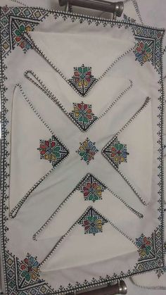 an embroidered white cloth with multicolored flowers and beads on the border is hanging from a metal frame