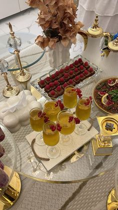 a table topped with desserts and drinks on top of a glass table covered in gold