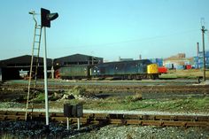 a train traveling down tracks next to a traffic light and other railroad tracks with buildings in the background