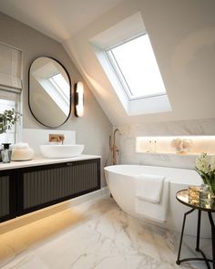 a white bath tub sitting under a bathroom window next to a sink and a mirror