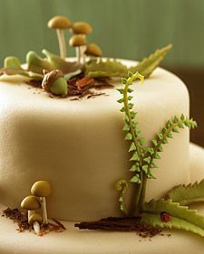 a close up of a cake with mushrooms and plants on the frosted icing