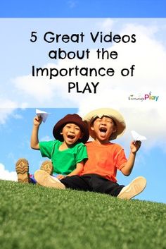 two young boys sitting on the grass with their arms in the air and one boy holding a paper airplane