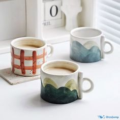 two coffee mugs sitting next to each other on top of a white countertop