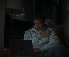 a man sitting on a couch in front of a laptop computer while wearing a robe