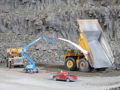 two toy trucks and a dump truck are in front of a rock wall with water pouring out of it