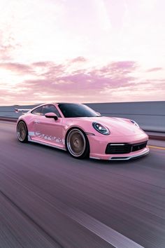 a pink sports car driving down the road at sunset or dawn with clouds in the background