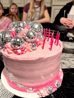 a birthday cake with pink frosting and decorations on top is surrounded by people in the background