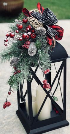 a candle holder decorated with pine cones, berries and evergreens is sitting on the ground