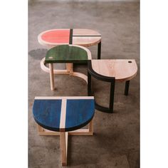 three tables made out of wood and different colored tops on concrete flooring, with one sitting in front of the other